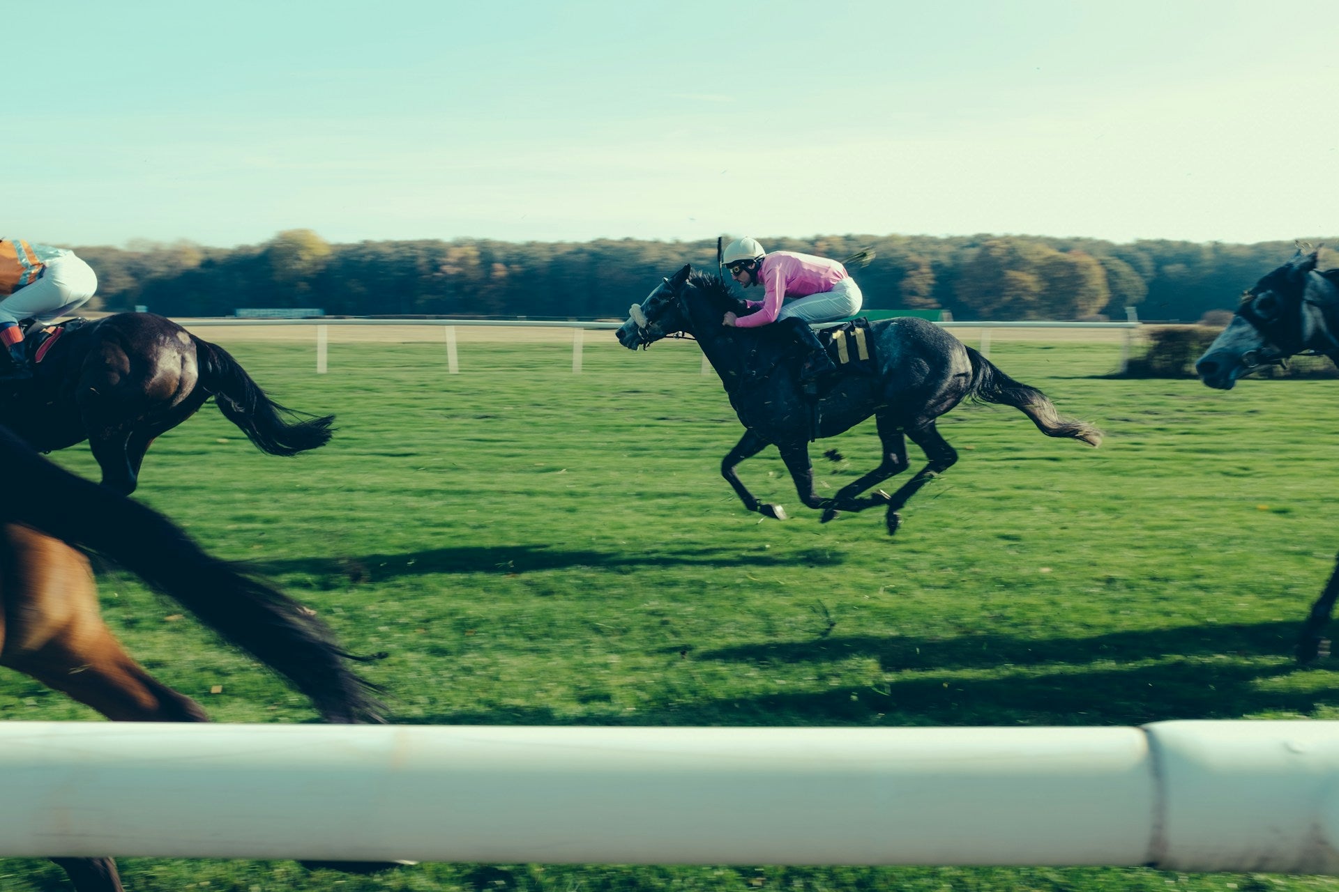 Horses racing on a grassy track with jockeys wearing hats.